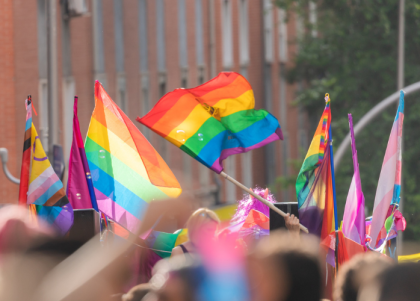 People waving colorful LGBTQ+ Pride flags at an outdoor Pride parade, celebrating diversity, inclusion, and LGBTQ+ rights.